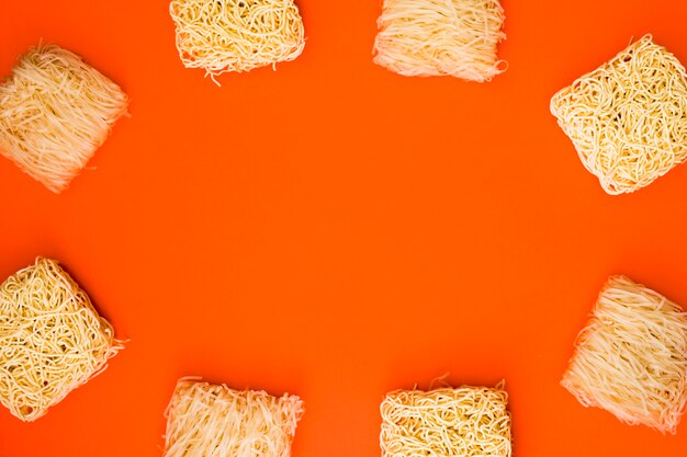 Frame made with variety of raw noodle blocks over orange background