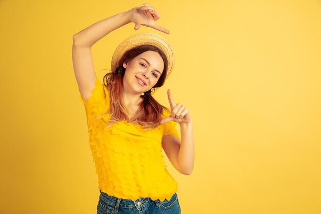 Framing, selfie, smiling. Caucasian woman's portrait on yellow studio background. Beautiful female model in hat. Concept of human emotions, facial expression, sales, ad. Summertime, travel, resort.