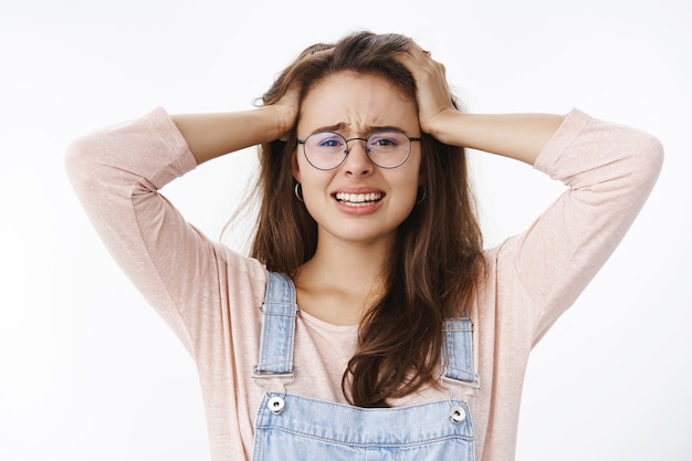 Freaked out woman panics holding hands on head frowning and clenching teeth