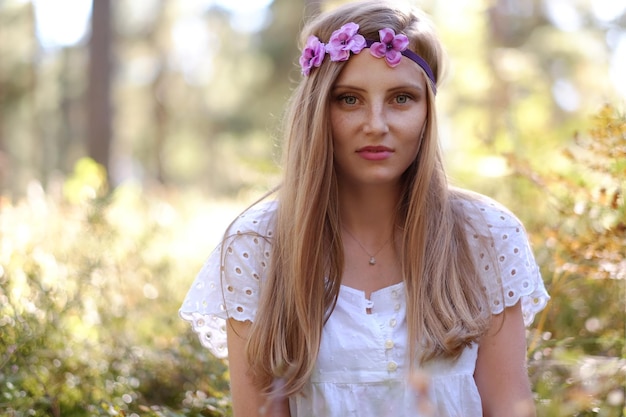 Freckled woman with circlet of flower on her head portrait in autumn forest in a day light.