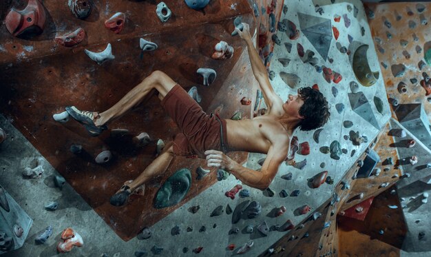 Free climber young man climbing artificial boulder indoors.