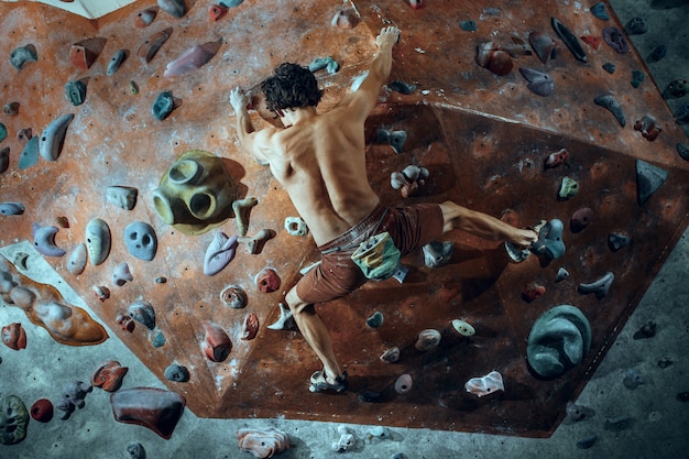 Free photo free climber young man climbing artificial boulder indoors.