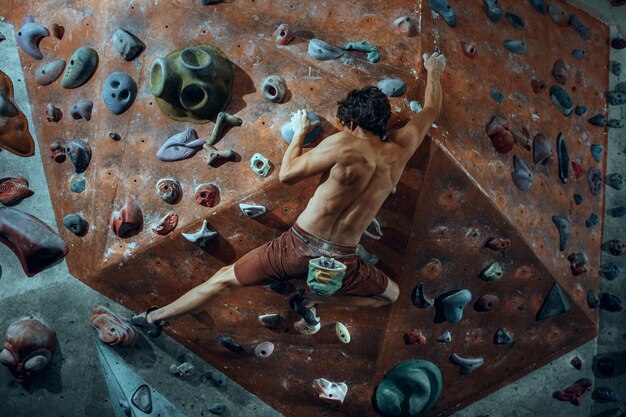 Free climber young man climbing artificial boulder indoors.