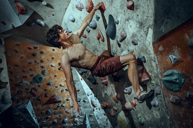 Free climber young man climbing artificial boulder indoors