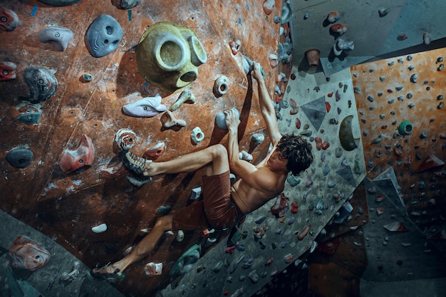 Free climber young man climbing artificial boulder indoors