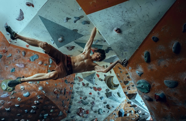 Free climber young man climbing artificial boulder indoors