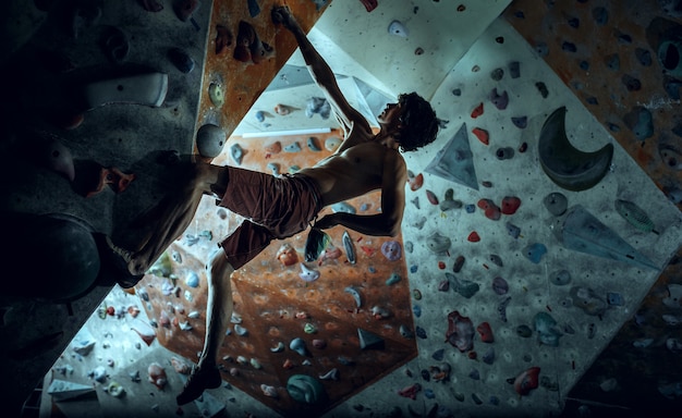 Free photo free climber young man climbing artificial boulder indoors