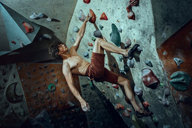 Free climber young man climbing artificial boulder indoors