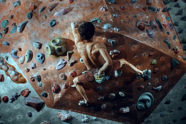 Free photo free climber young man climbing artificial boulder indoors