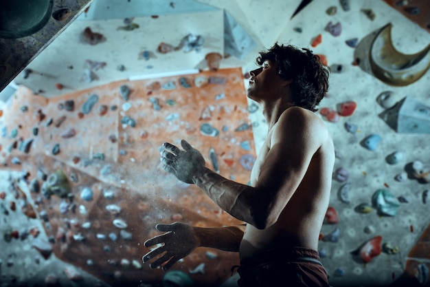 Free climber young man climbing artificial boulder indoors