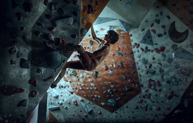 Free climber young man climbing artificial boulder indoors