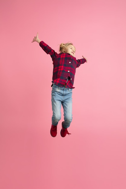 Free and happy, flying, jumping high. Caucasian girl's portrait on pink wall. Beautiful model with blonde hair.