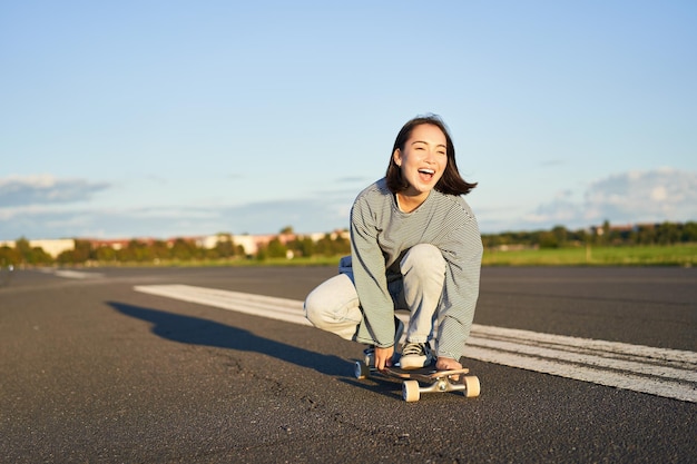 Свобода и счастье счастливая азиатская девушка катается на своей длинной доске по пустой солнечной дороге, смеясь и улыбаясь