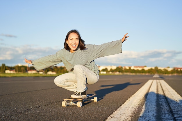 自由と幸福空の晴れた道でロングボードに乗って幸せなアジアの女の子が笑い、笑顔でスケートボードをする