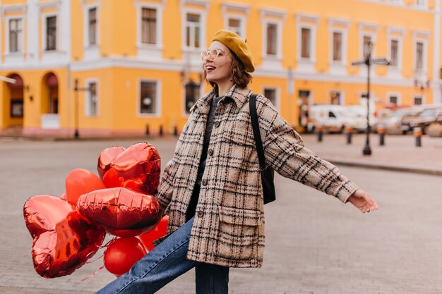 ジーンズと黄色いベレー帽の自由を愛する女性は、街を散歩するのを楽しんでいます