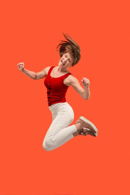 Freedom in moving. Mid-air shot of pretty happy young woman jumping and gesturing against orange studio background. Runnin girl in motion or movement. Human emotions and facial expressions concept