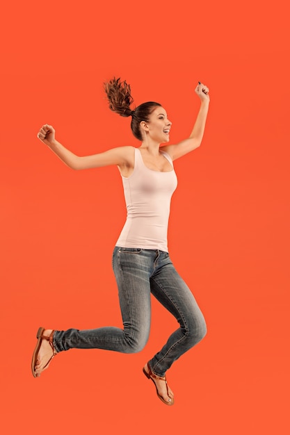 Freedom in moving. Mid-air shot of pretty happy young woman jumping and gesturing against orange studio background. Running girl in motion or movement.