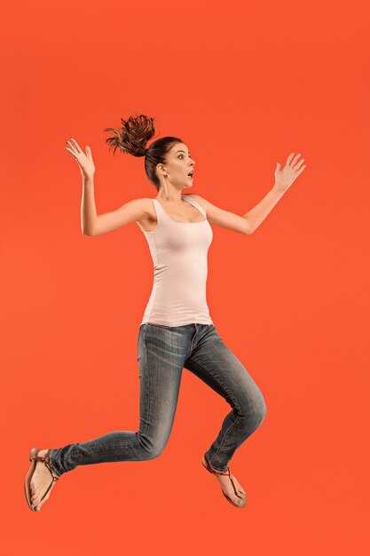 Свобода передвижения. В воздухе выстрел довольно счастливая молодая женщина прыгает и жестикулирует на оранжевом фоне студии.