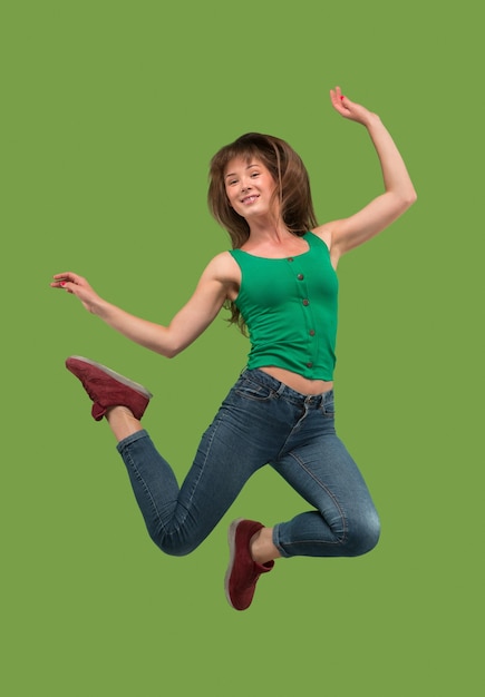 Free photo freedom in moving. mid-air shot of pretty happy young woman jumping and gesturing against orange studio background.