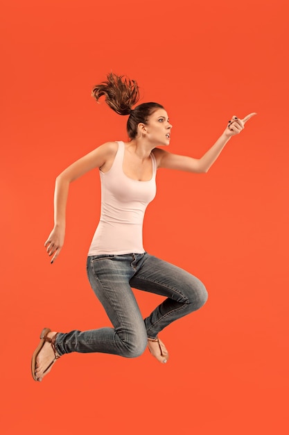 Freedom in moving. Mid-air shot of pretty happy young woman jumping and gesturing against orange studio.