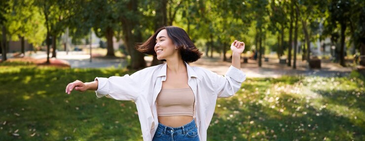 無料Photo 自由と人のコンセプト、笑顔で楽しんで木の周りの公園で踊る幸せな若いアジアの女性