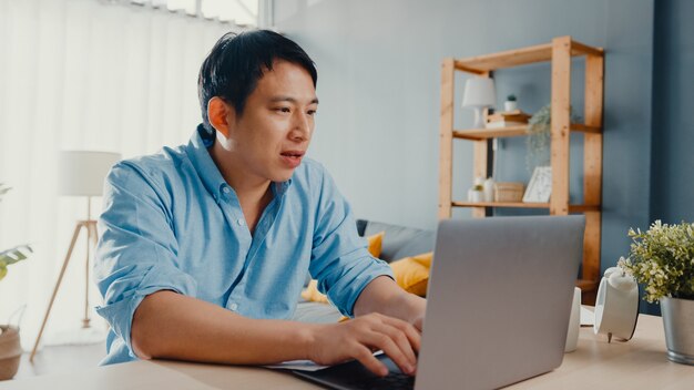Freelance Asia guy casual wear using laptop online in living room at home office