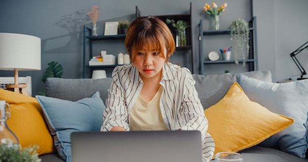 Abbigliamento casual donna asiatica freelance utilizzando l'apprendimento online del computer portatile nel soggiorno di casa