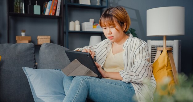 Freelance asian lady casual wear using tablet online learning in living room at house