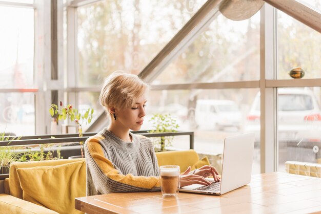 コーヒーショップでノートパソコンを扱うフリーランスの女性