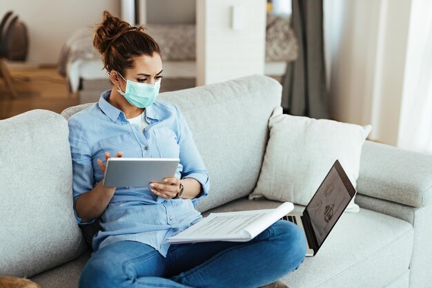 Freelance worker with face mask using digital tablet while going through business reports at home