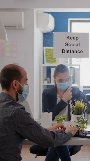 Freelancer with protection medical face mask working on laptop computer while talking on phone with team