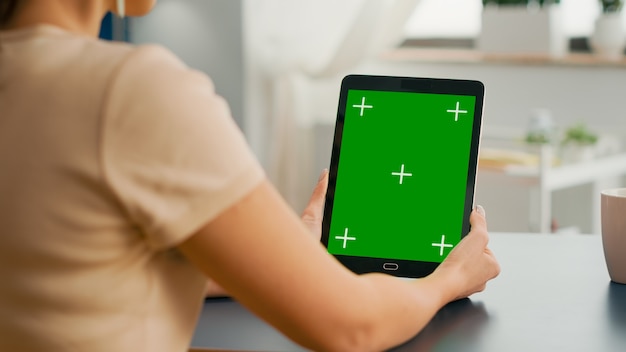 Freelancer woman holding tablet computer with mock up green screen chroma key display sitting on office room. Caucasian female browsing on internet for online project using isolated device