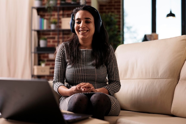 Freelancer working on laptop with headphones and listening to music or podcast. Attending online webinar lesson or enjoying song while she does remote business work on computer at home.