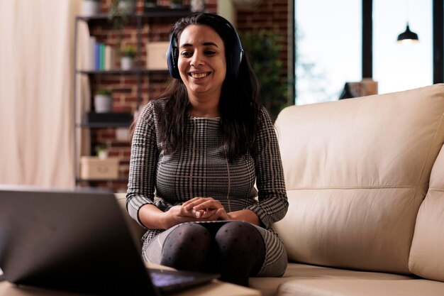 Freelancer working on laptop with headphones and listening to music or podcast. Attending online webinar lesson or enjoying song while she does remote business work on computer at home.