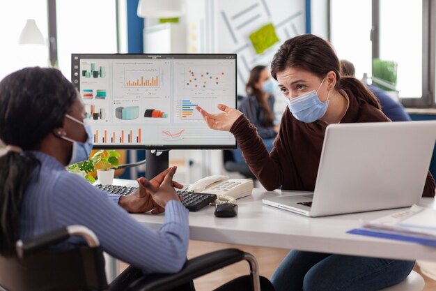 Freelancers wearing protective face masks working on computer in business office during global pandemic