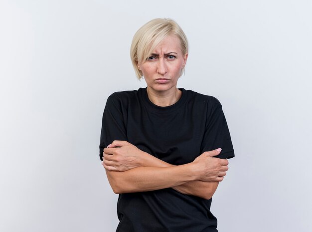 Freezing cold middle-aged blonde woman keeping hands crossed on arms looking at front isolated on white wall