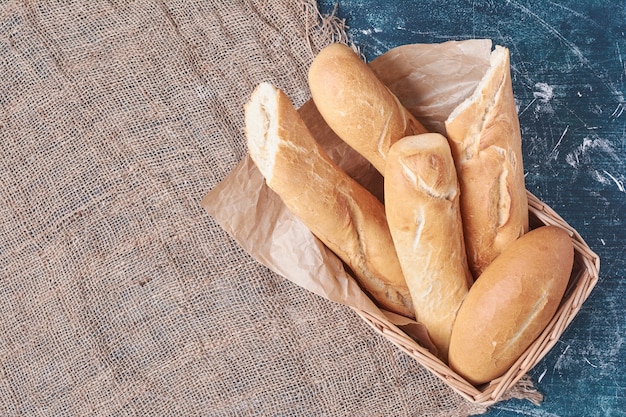 French baguettes in a basket on blue table.