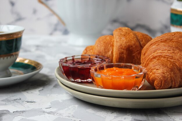 Французский завтрак с круассанами, абрикосовым джемом, вишневым джемом и чашкой чая, красными и желтыми цветами