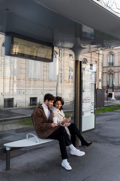 French couple waiting at the station to take the bus and drinking coffee