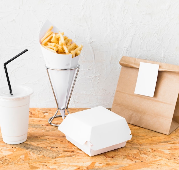 Картофель-фри; чаша для удаления; и пакет продуктов питания на деревянном столе