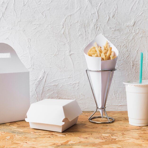 French fries; disposal cup and food parcel on wooden desk