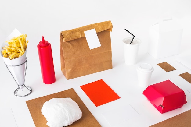 French fries; disposal cup; sauce bottle and food packages on white table top