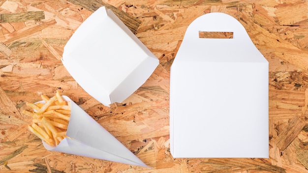 French fries in paper cone and white package on wooden background