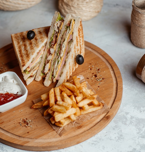 French fries with club sandwiches served with sauces on a wooden board