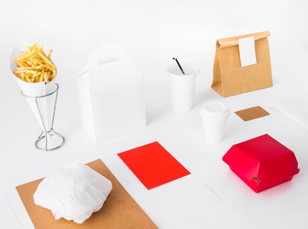 Free photo french fries with food packages and disposal cup on white backdrop