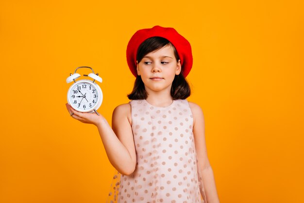french kid in stylish beret. Caucasian child posing on yellow wall with clock.