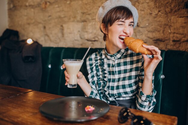 Free photo french woman in cafe drinking latte and eating croissant