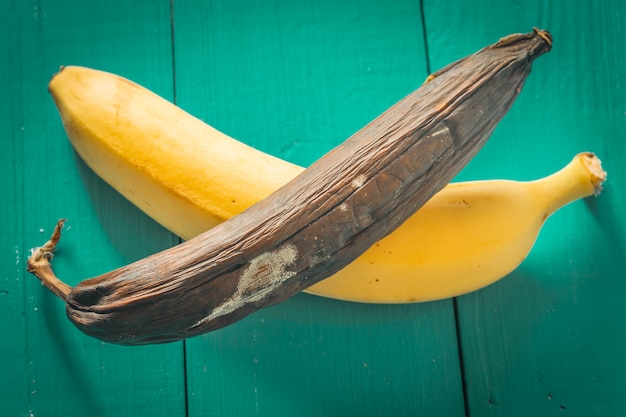 Свежий и гнилой банан на деревянном фоне