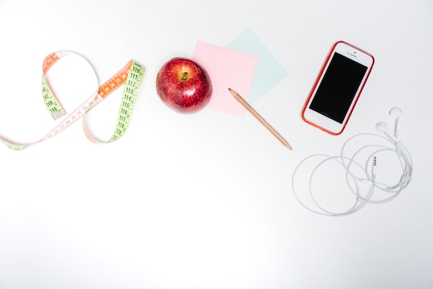 Fresh apple; measuring tape; adhesive notes and smartphone on white backdrop