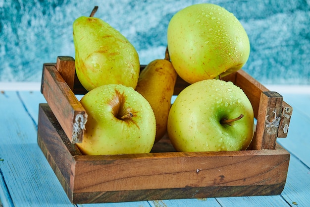 Mele e pere fresche in una scatola di legno sulla superficie blu.